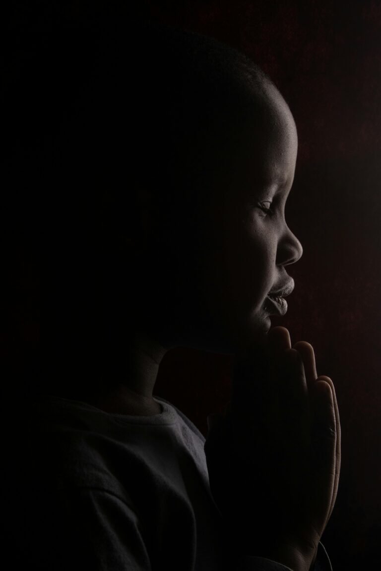 A moving portrait of a child praying, captured in silhouette with dramatic lighting.