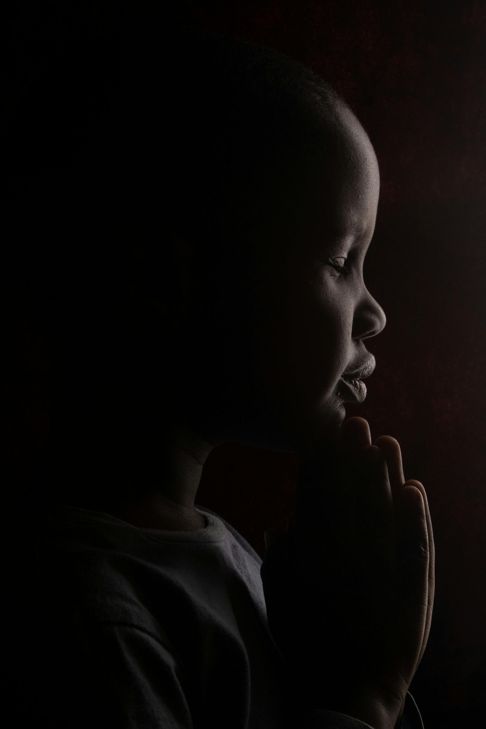 A moving portrait of a child praying, captured in silhouette with dramatic lighting.