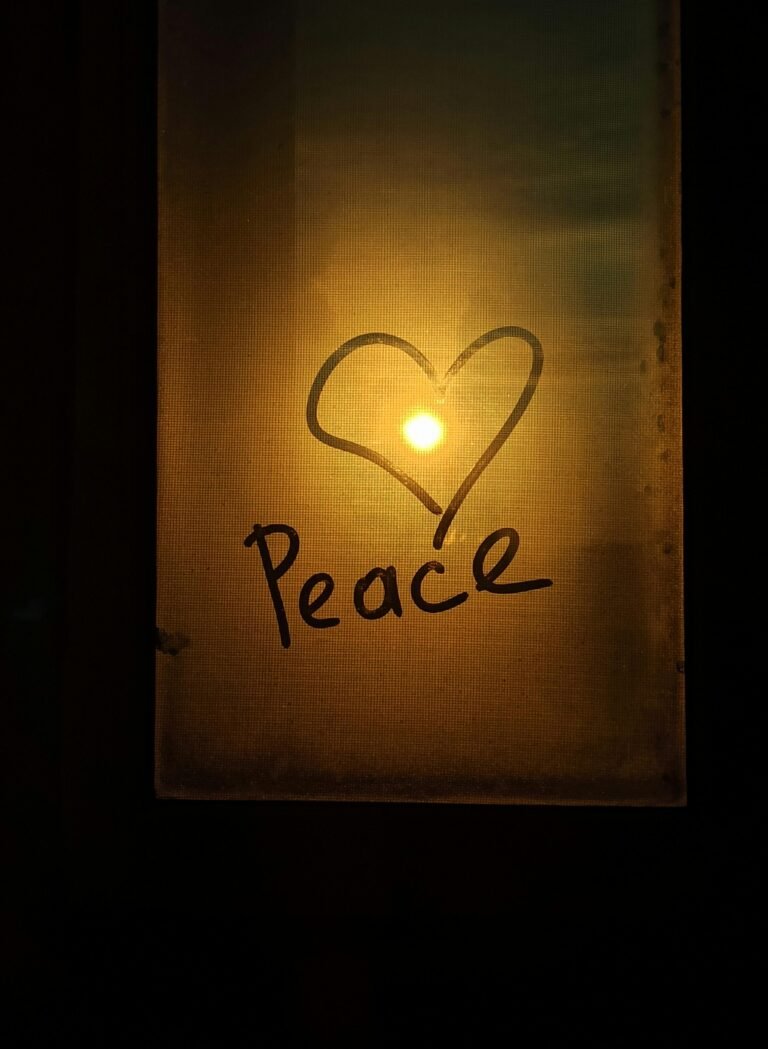 A heart and the word peace drawn on a glass panel with the sunset in the background.