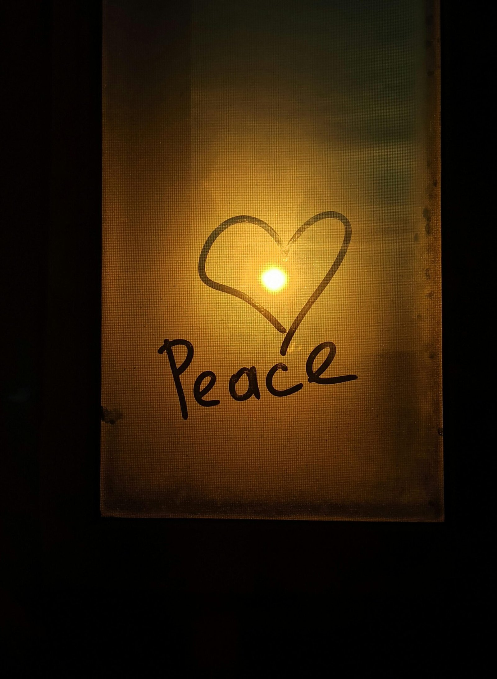 A heart and the word peace drawn on a glass panel with the sunset in the background.